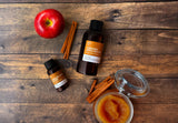 fragrance oil bottles on wood background with apple butter, cinnamon, and a red apple.
