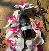 Black Poppy oil bottle on a wooden surface with flowers and vanilla beans.