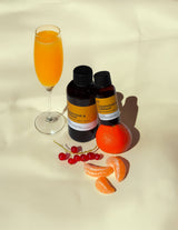 Two bottles of 'Clementine & Currant' with an orange cocktail and fruit on a beige background