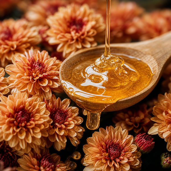 Golden honey being poured into a wooden spoon, surrounded by dried orange and brown flowers.