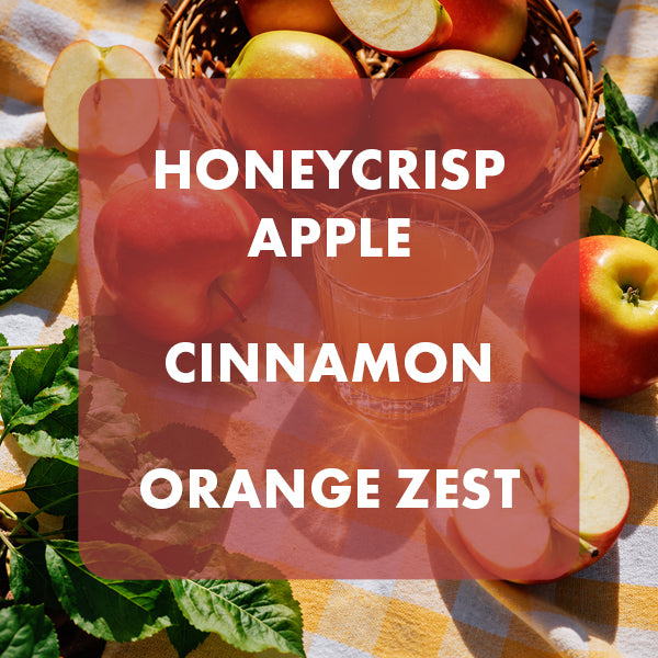 A styled flat-lay of fresh honeycrisp apples, a glass of orange juice, cinnamon sticks, and orange zest on a yellow-and-white checkered cloth, with a translucent red overlay reading 'HONEYCRISP APPLE CINNAMON ORANGE ZEST'.