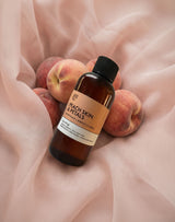 Bottle of 'Peach Skin & Petals' Fragrance2U fragrance oil surrounded by peaches on a soft fabric background