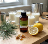 Bottle of Pinesap & Yuzu Fragrance2U fragrance oil with candles, lemons, and pine branches on a wooden surface.
