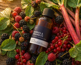 Bottle of 'Berries & Brambles' on a bed of fresh berries and rhubarb