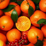 Oranges with one sliced open, surrounded by red berries, on a green leafy background.