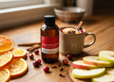 Bottle of cran apple toddy Fragrance2U fragrance oil with oranges, apples, and a mug on a wooden table.