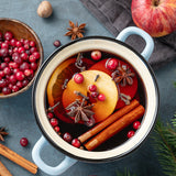 Spiced fruit mixture in a white pot with apples, oranges, and spices on a dark surface.