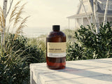 Bottle of Dune Grass Fragrance2U fragrance oil on a wooden surface with a scenic beach background