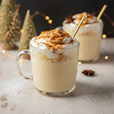 Two glasses of eggnog with whipped cream and a gold straw on a festive background.