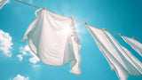 Sun shining though clean laundry drying on a line. A background of a bright blue sky with a few clouds.