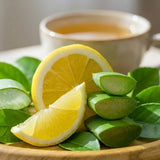 Lemon slices and lime wedges on a wooden plate with a blurred cup of tea in the background.