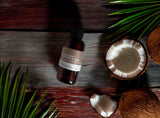 Bottle of Mahogany Coconut & Teak Fragrance2U fragrance oil on a wooden surface with coconuts and leaves.