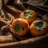 Three persimmons on a brown fabric background