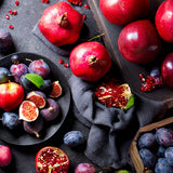 Assorted fruits including pomegranates, apples, figs, and plums on a dark surface.