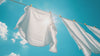White sheets wave in the wind hanging on a clothing rack. A bright blue sky with shining sun in the background.
