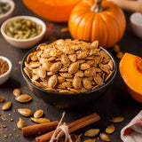 Bowl of roasted pumpkin seeds with pumpkins and cinnamon sticks on a dark surface