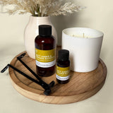 Two bottles of salty amber & orange blossom and a candle on a wooden tray with a vase of dried flowers in the background.