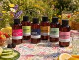 set of fragrance2U fragrance oil bottles on a table outdoors with strawberries, cucumbers, lemons, and flowers